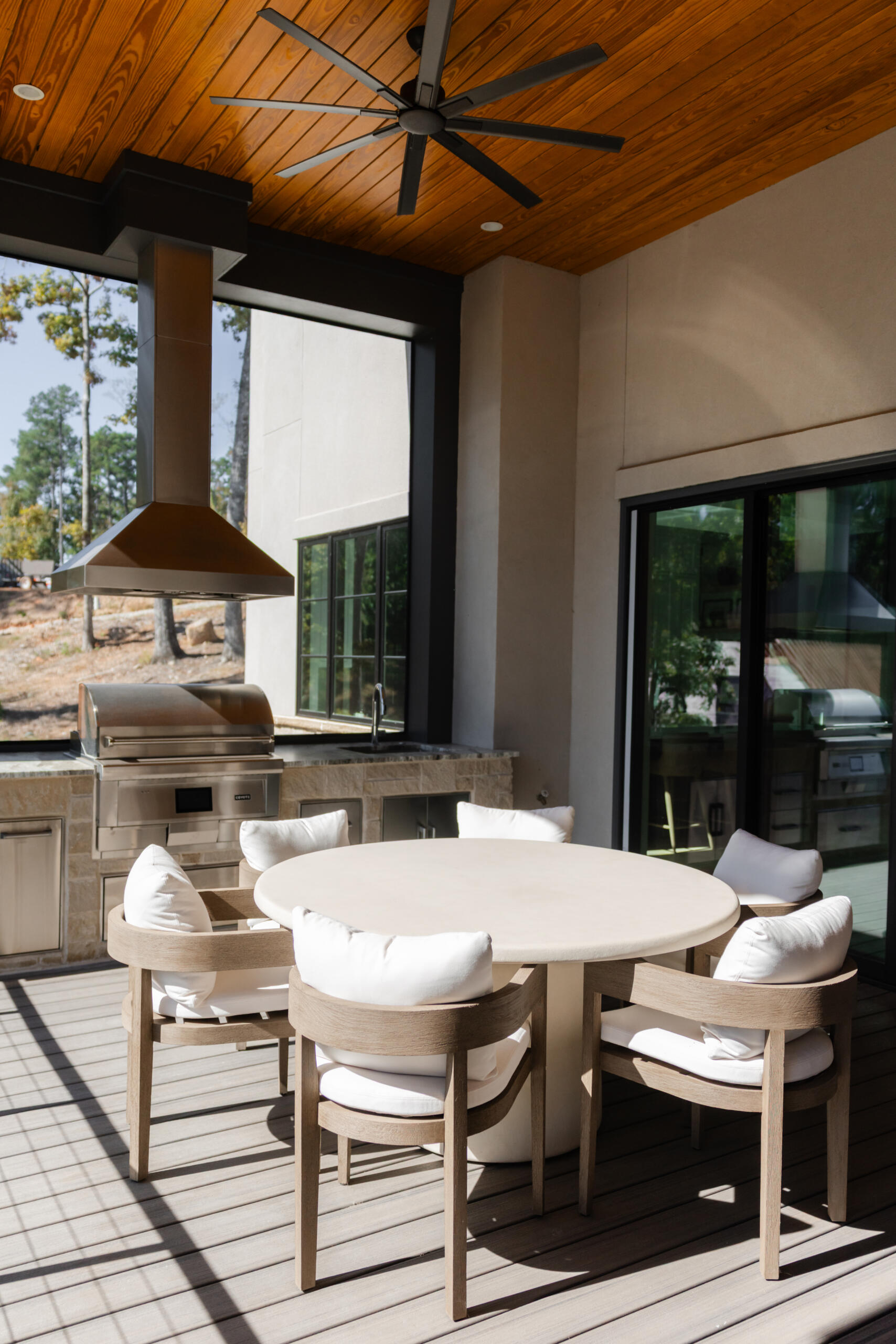 Luxury outdoor covered patio with wood ceiling, ceiling fan, round dining table, and outdoor kitchen with grill - Southern Luxury Homes